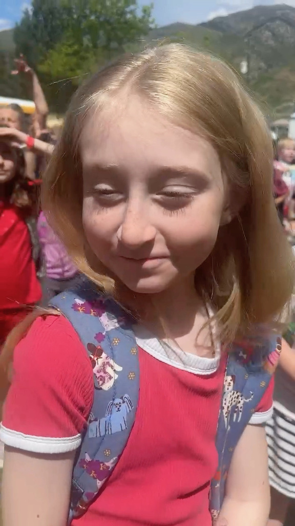 Blonde female student in red shirt smiling in front of school