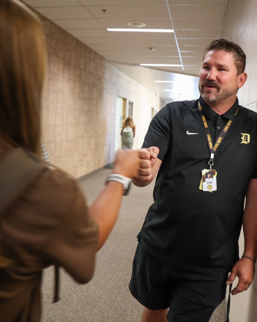 A teacher greeting a student into class by giving them knuckles.