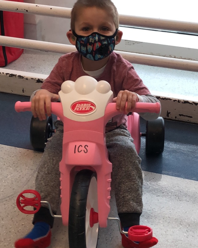 A student wearing a mask while riding a tricycle.