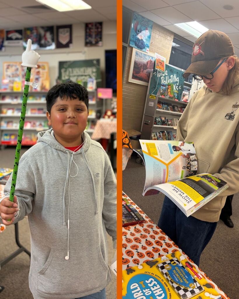 two students looking at books and holding a long pointer finger during the book fair