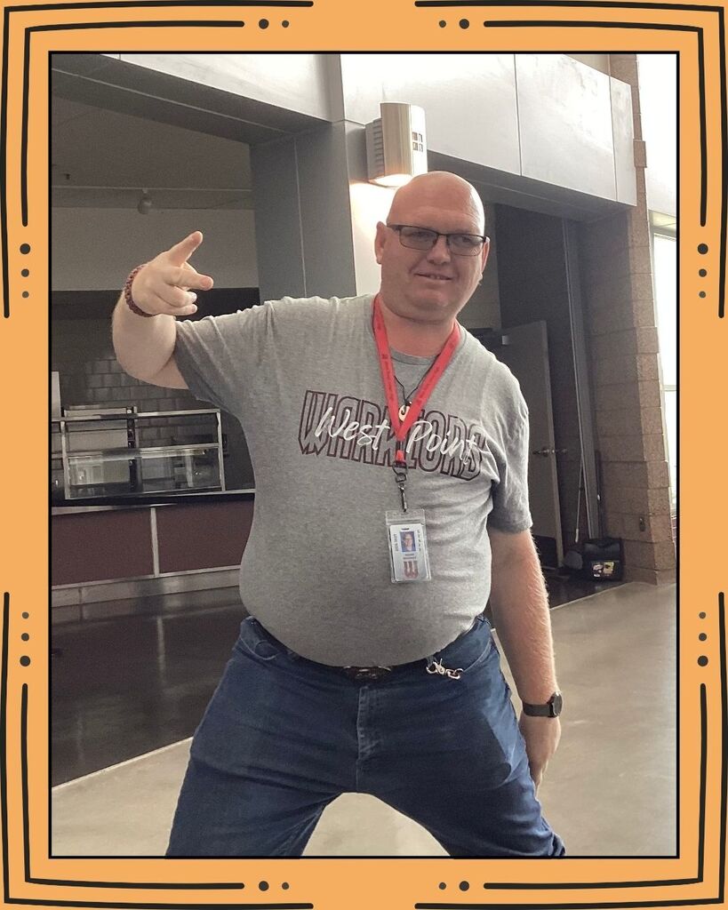 A janitor wearing a gray shirt posing for a picture in the cafeteria.