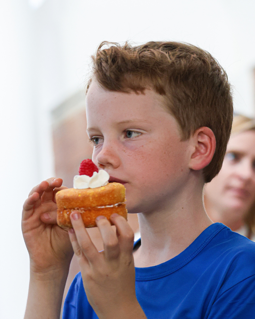 A student holding up a small cake with a raspberry up to their face. 