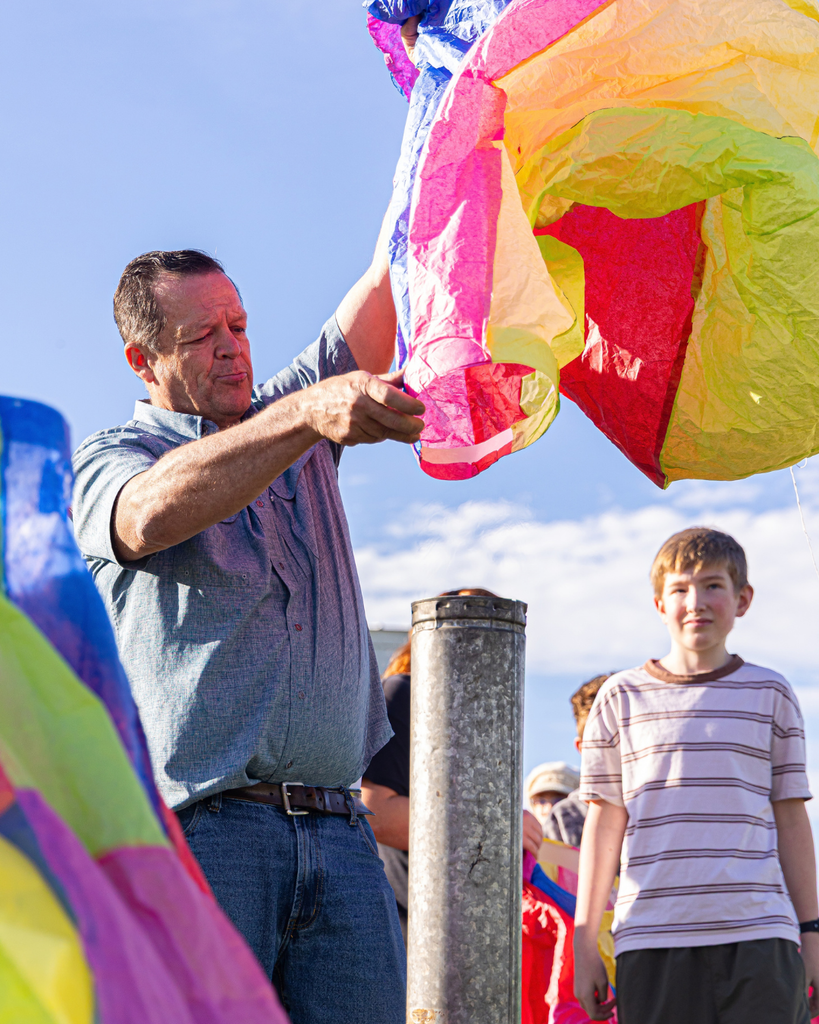 A teacher putting a student's hot air balloon project on a pipe. 