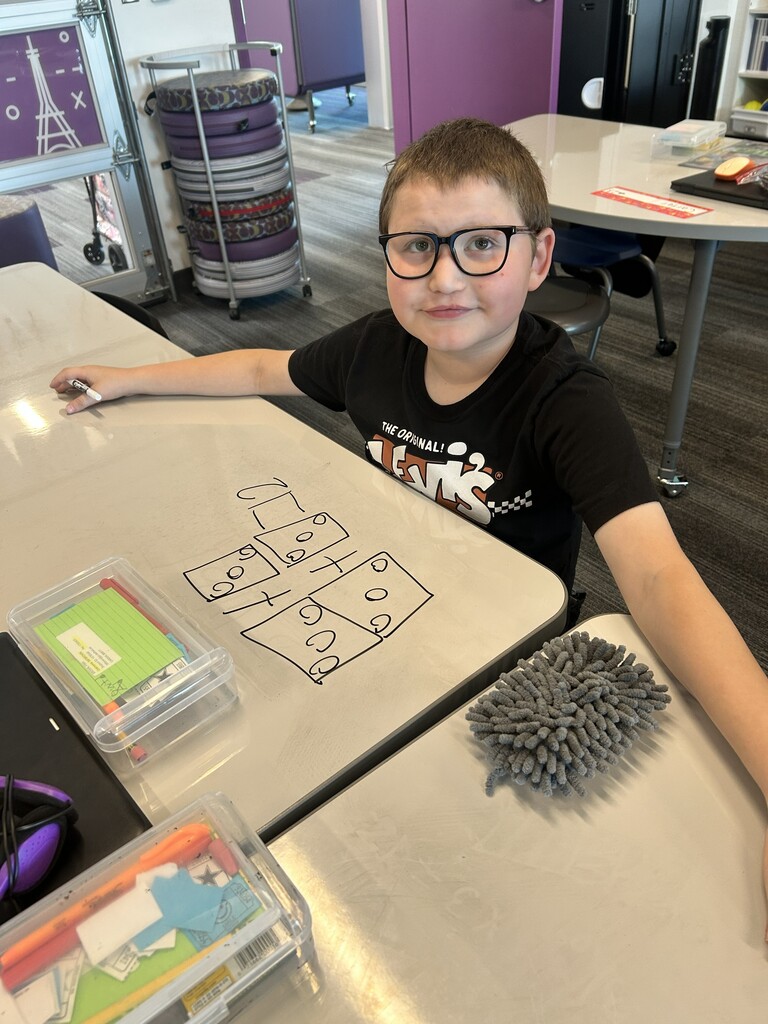 a boy with glasses with boxes and dots drawn inside is on his desk in front of him