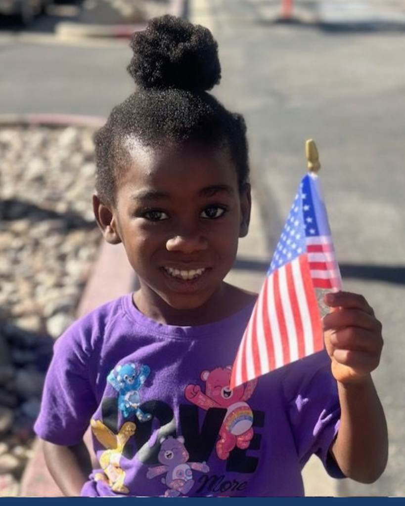 A student smiling while holding an American flag. 