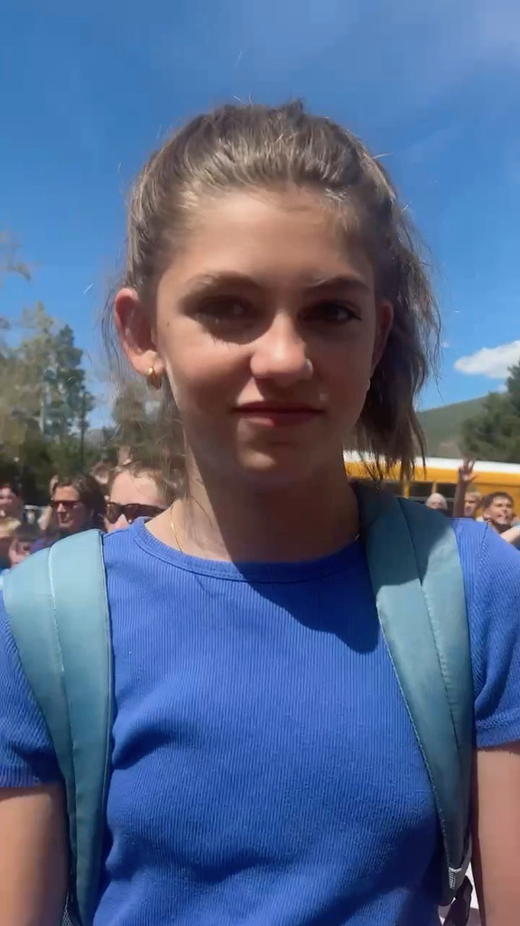 6th grade girl in blue shirt and green backpack with a ponytail standing outside her school