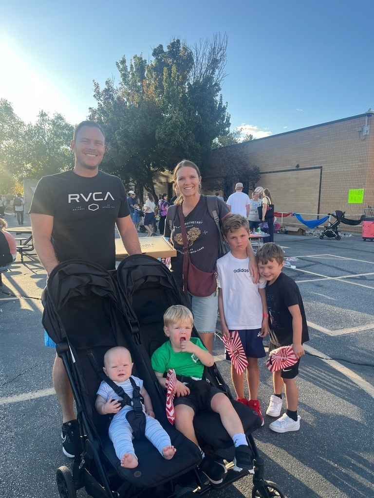A mother and father with their four children are smiling and at their local elementary school's carnival.