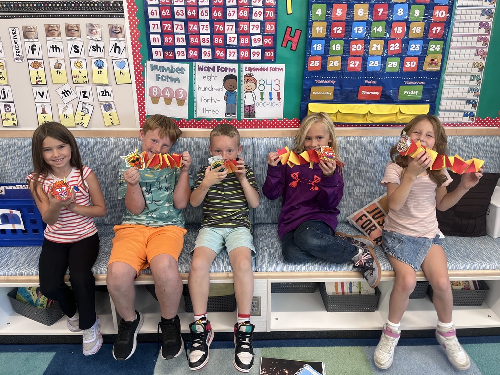 five students holding yellow and red paper dragons while sitting on a bench