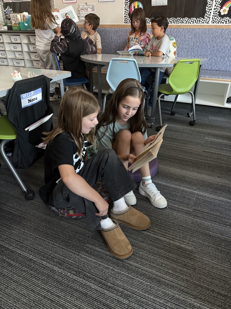 two girls reading from the same book while sitting on the ground
