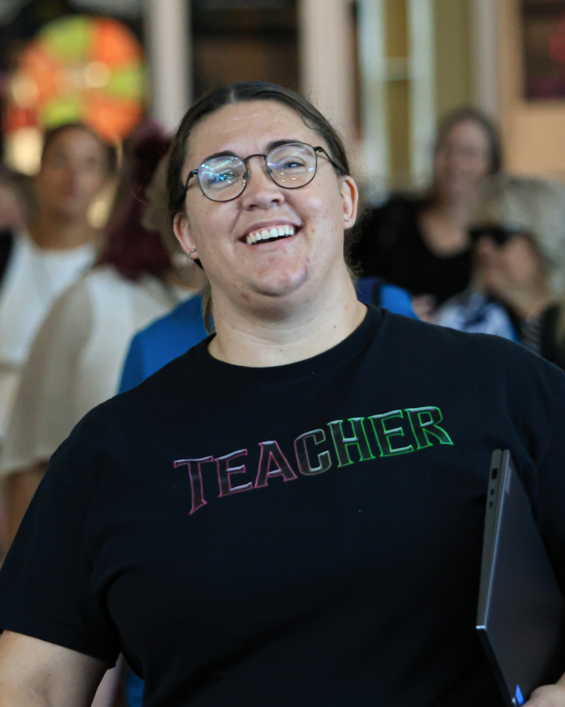 A person in a black "teacher" shirt smiles. 