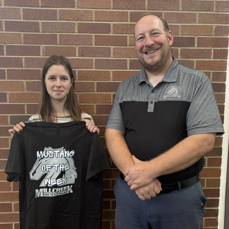 student holding a Mustang of the week shirt with principal