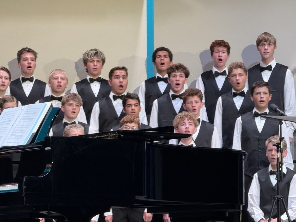 Male students singing in white shirts and black vests. 