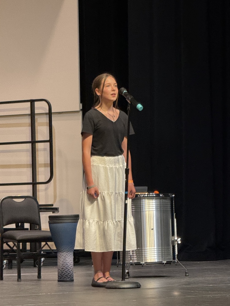 Student singing a solo wearing a black shirt and white skirt. 