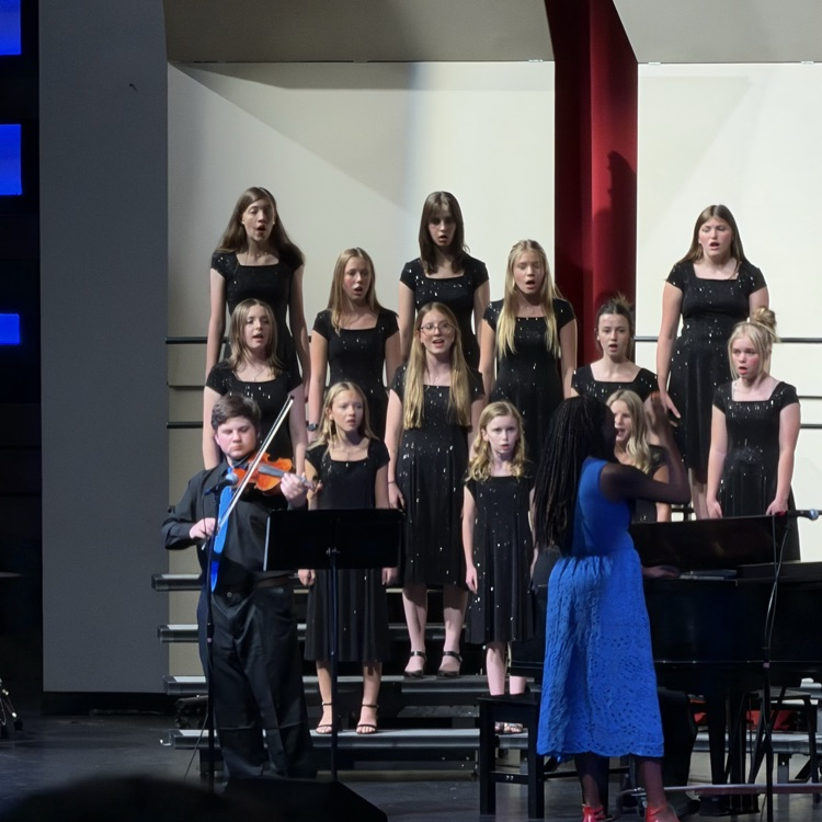 a large group of junior high students stand on risers and sing for a crowd
