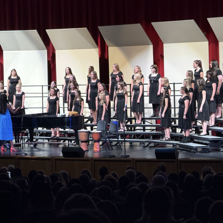 a large group of junior high students stand on risers and sing for a crowd