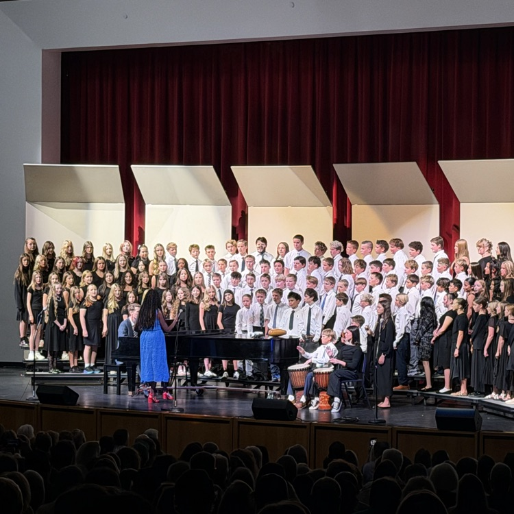 a large group of junior high students stand on risers and sing for a crowd