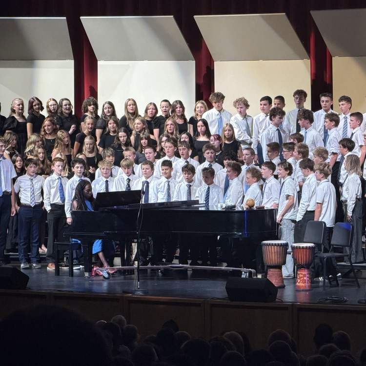 a large group of junior high students stand on risers and sing for a crowd