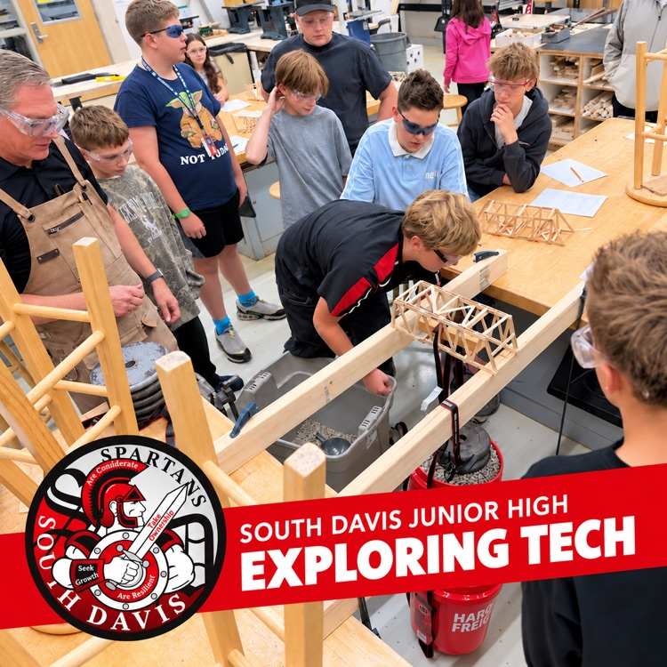 Students and their teacher gather around a workbench to test student-built bridges in Exploring Tech class.