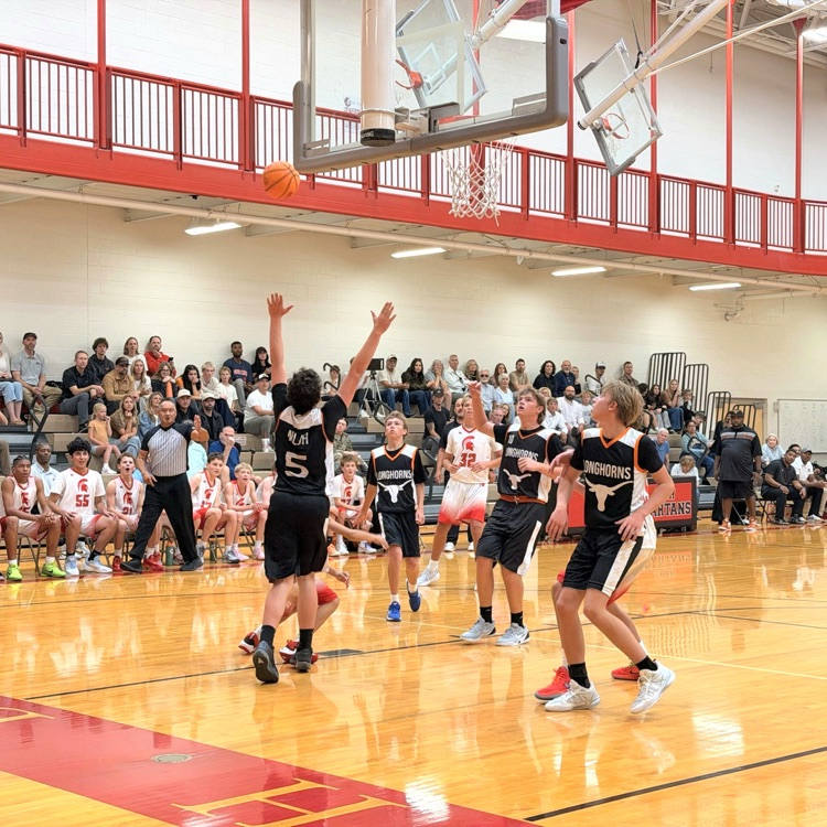 A basketball player shoots near the basket as teammates and opponents watch.