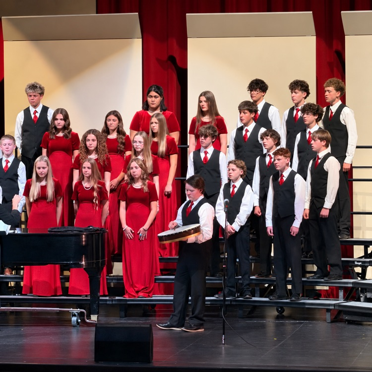 Choir students dressed in red and black perform with a student playing a drum.