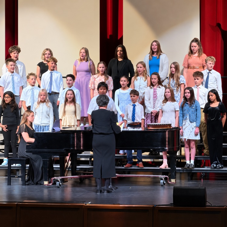 Beginning choir students sing alongside a pianist and conductor.