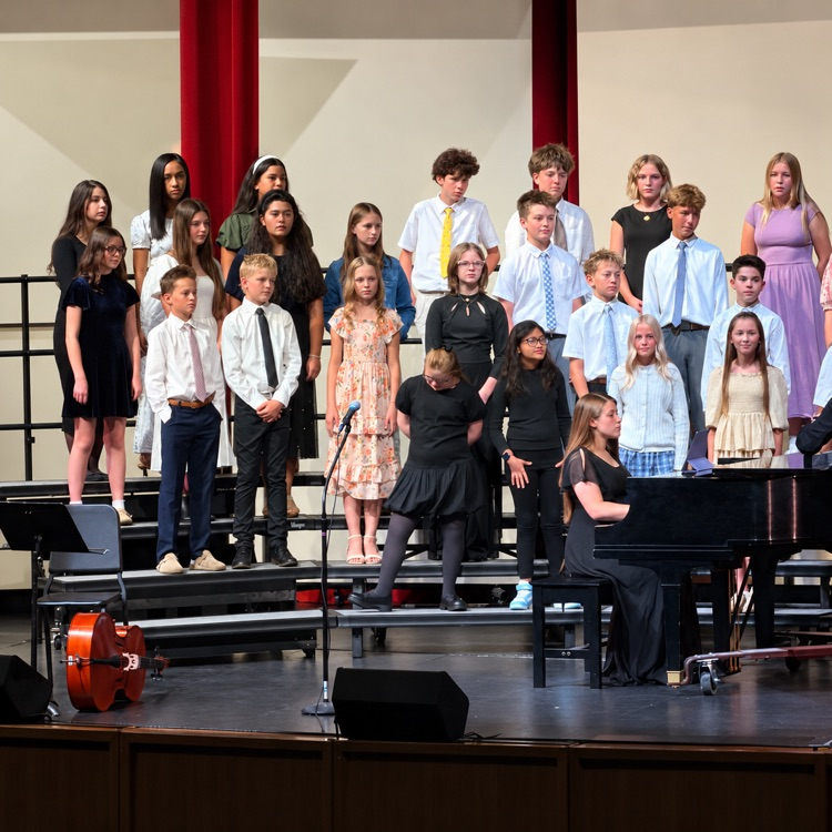 Beginning choir students perform on stage with piano accompaniment.