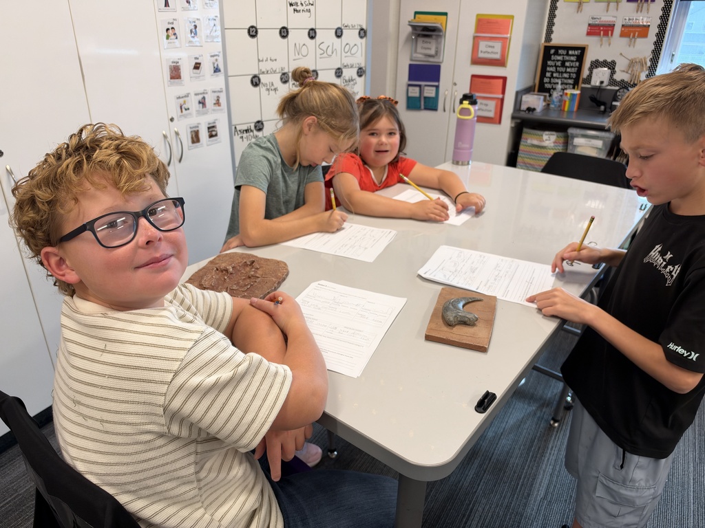 a boy with glasses and two girls at a table with a dinosaur print and claw