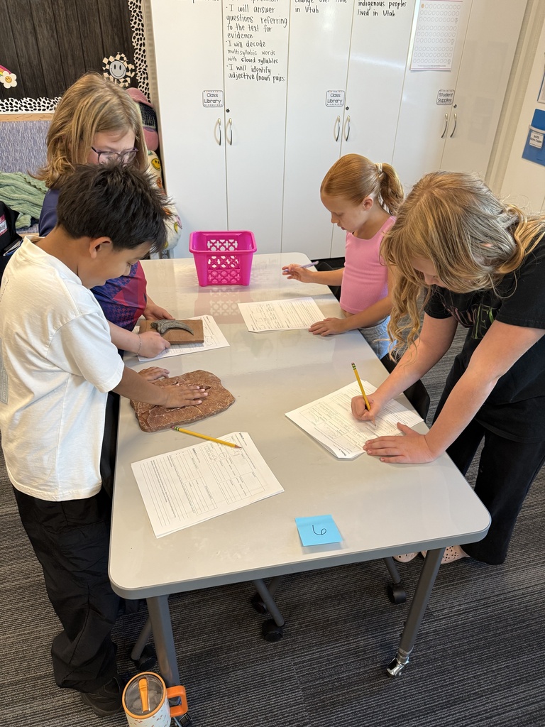 4 students standing around the table with papers and a boy putting his hand inside a dinosaur print