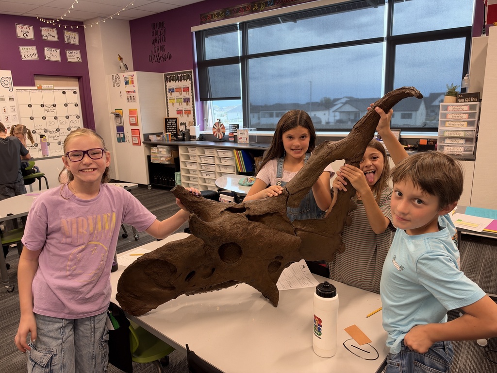 four students holding up a large replica model of a horned dinoasaur