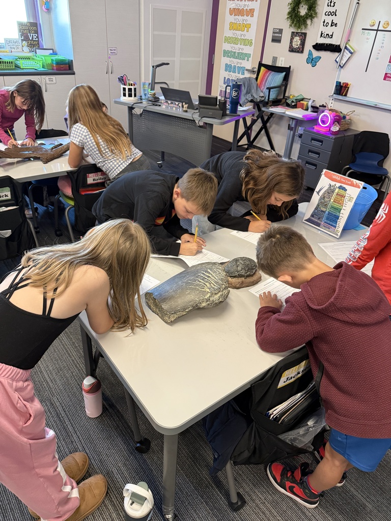 a group of students writing down things on paper with replica fossils in the center of the table. One fossil has scratch marks on it