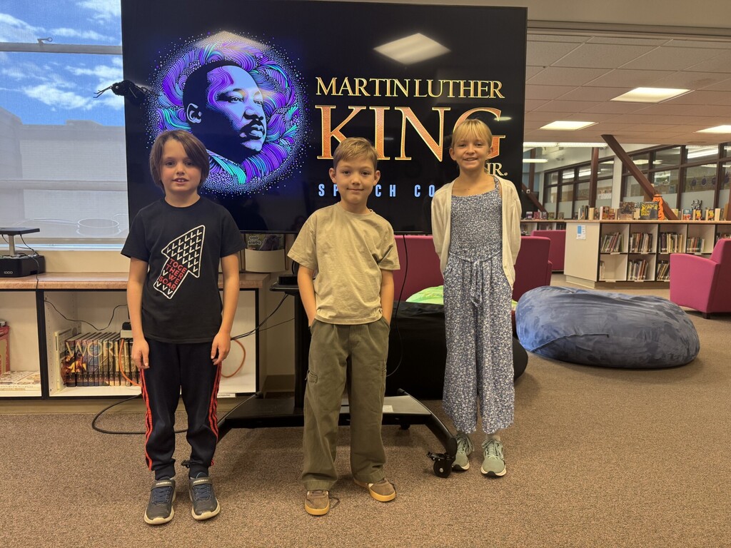 3 students standing in front of a picture of Martin Luther King Jr. on a TV.