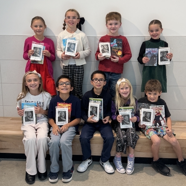 Nine Bountiful Elementary students who participated in the Martin Luther King Jr. Contest pose together for a group photograph. Four students stand behind five classmates seated on a wooden bench. Each student holds a book or booklet accompanied by a printed sheet featuring a photograph of Dr. Martin Luther King Jr. The students smile proudly at the camera.