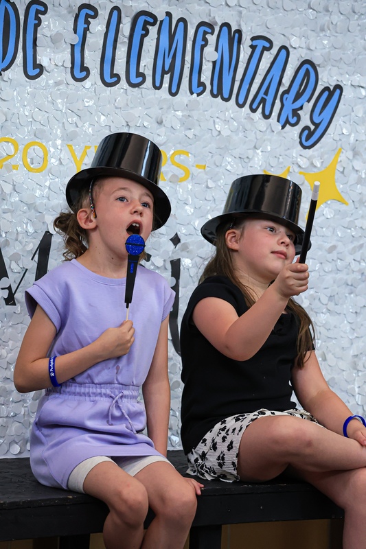 Two students sitting in front of a confetti banner wear hats and hold up photo props.