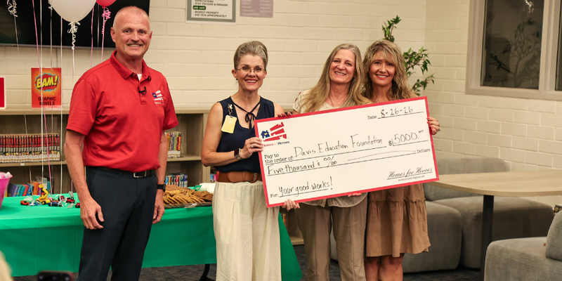 Four people smiling at the camera holding a large check made out to the Davis Education Foundation for 5,000 dollars.