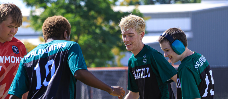 Students playing soccer together smiling.