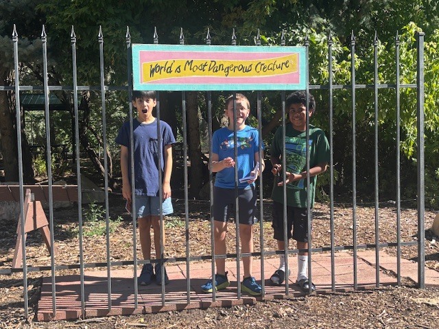 Three students stand behind a fence under a sign that says, "World's Most Dangerous Creature".