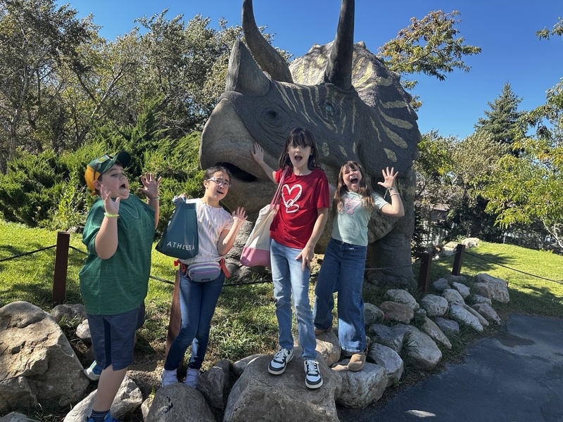 Four students pose next to a sculpture of a triceratops.