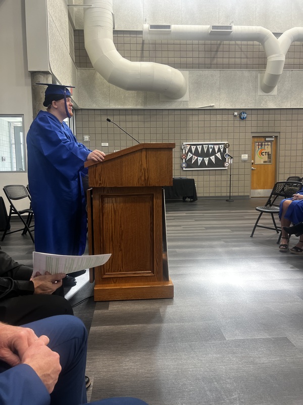 A student stading at a podium with a microphone speaking in front of an audience