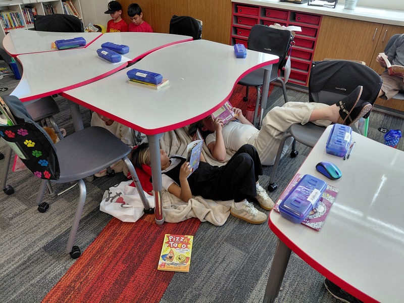 Students laying under a table reading their books.