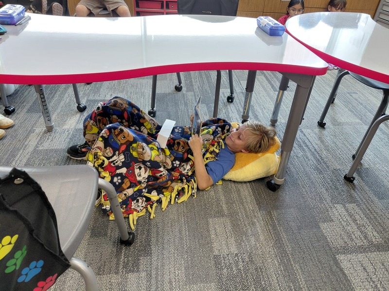 Student laying under a table reading a book.