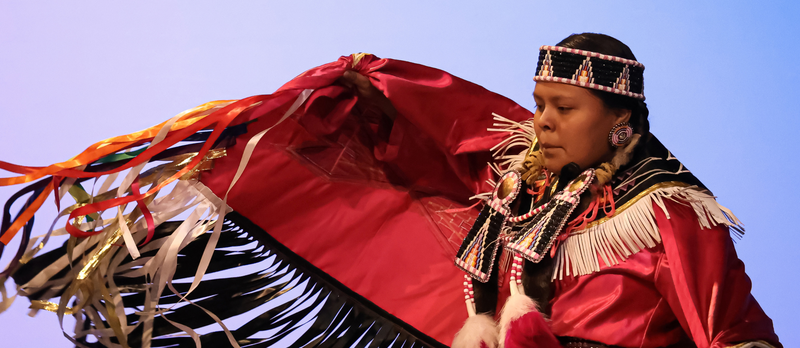 A student dancing in their traditional Native American clothing.