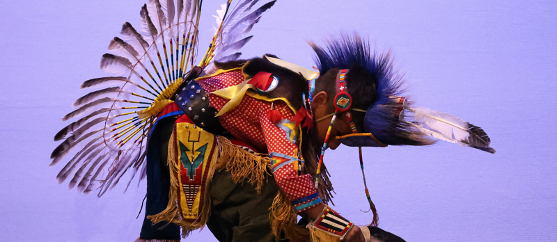 A student dancing in their traditional Native American clothing.