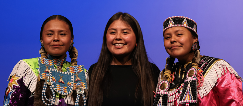 Students dressed in Traditional Native American clothing pose with one person.