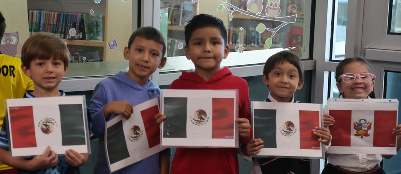Students holding up images of the Mexico flag and smiling.