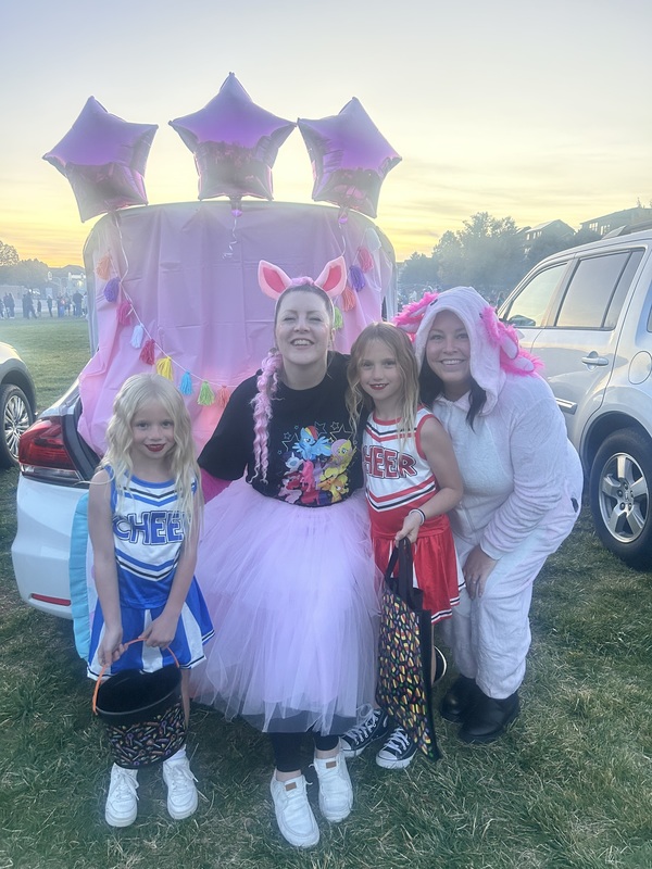 Office staff with 2 students in front of decorated trunk