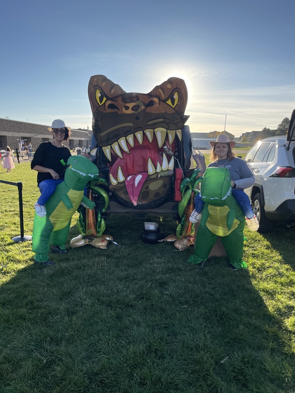 Recess coaches dressed in dinosaur blowups in front of dinosaur trunk