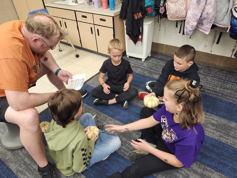 Parent helping students play a game at a Halloween party.