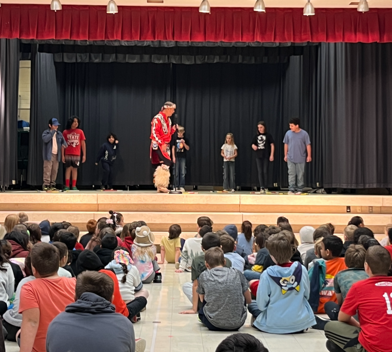 hoop dancer with meadowbrook students on stage trying out hoop dancing skills