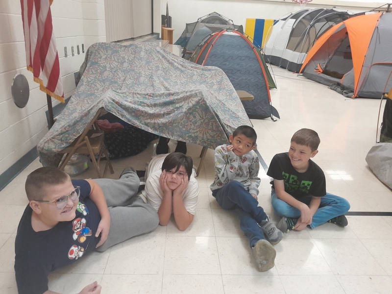 Students in the gym in front of a blanket fort along with tents