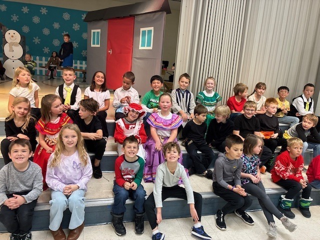 Students sitting on the stage dressed for the play.